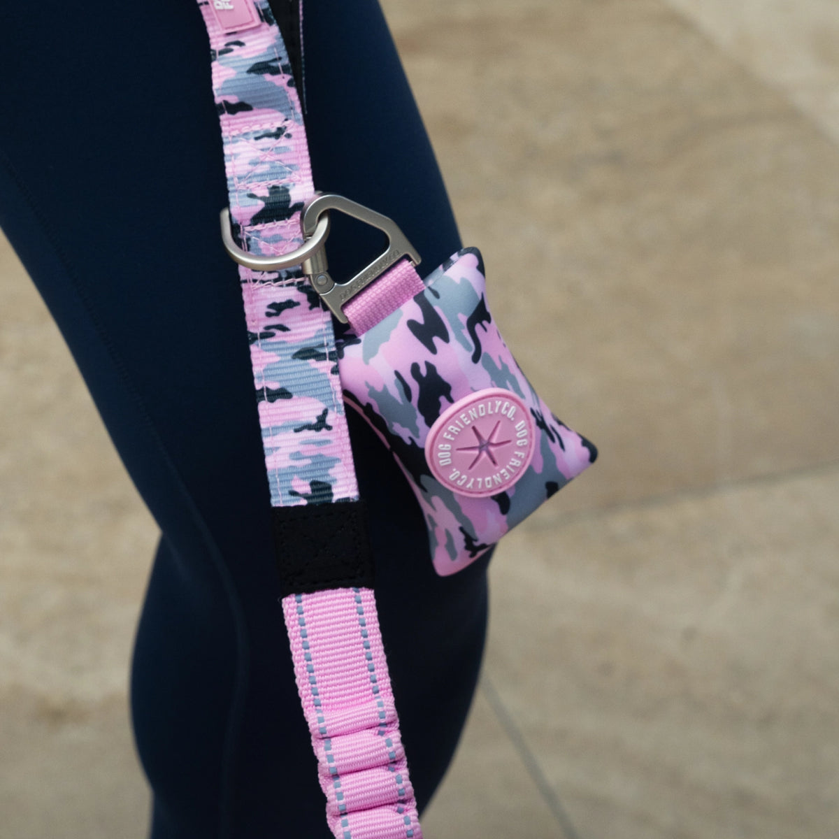Person holding a Pink Camo bungee dog leash with poop bag holder.
