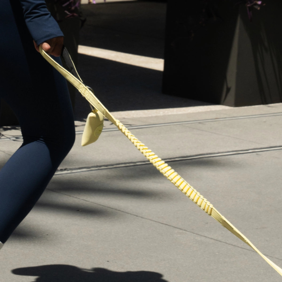 Person holding a yellow bungee dog leash while walking a dog.