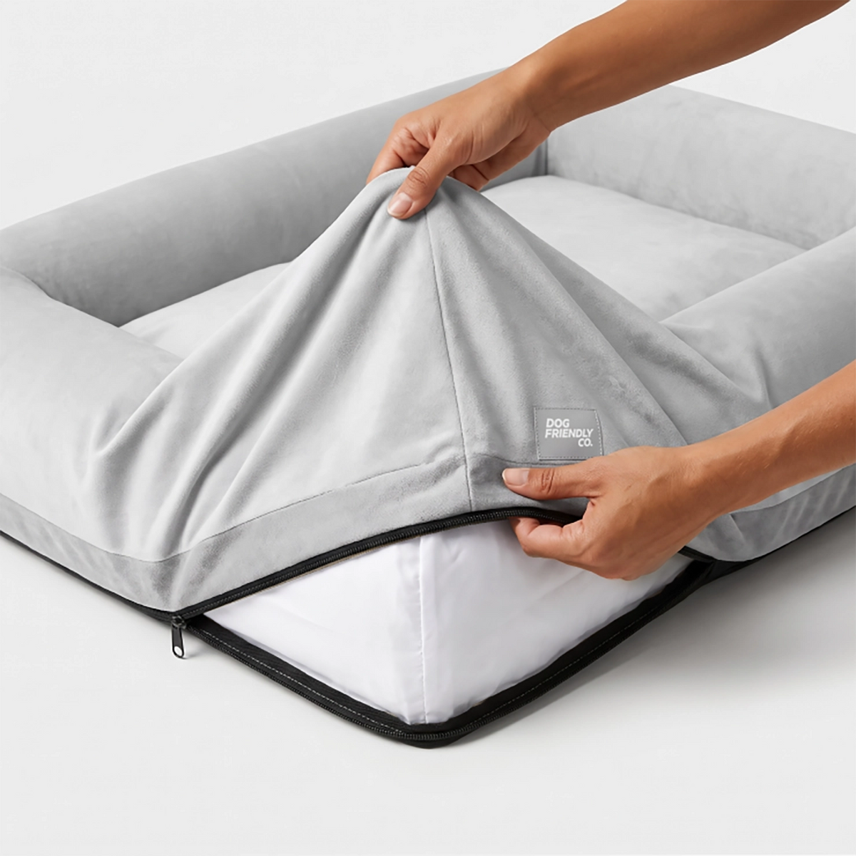 Grey replacement cover being lifted from a Dog Friendly Co. dog bed to show the zipper and inner bed.