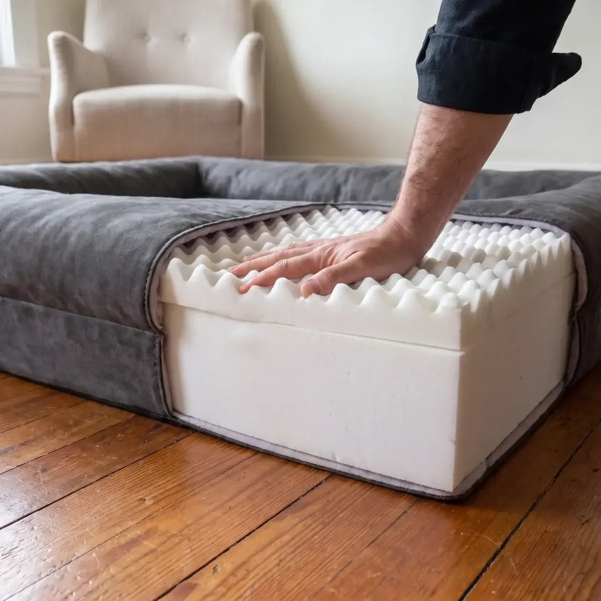 A hand pressing the egg-crate memory foam top of the cut-open bed, the firm white base underneath